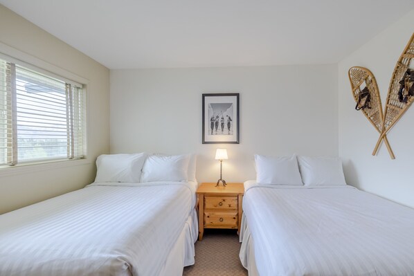 Une chambre double avec deux lits, une table de chevet avec une lampe, un tableau encadré au mur et une décoration murale en fibres tressées.