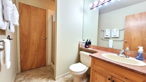 Une salle de bain avec une porte en bois, des toilettes, un lavabo avec un miroir et des articles de toilette posés sur le comptoir.
