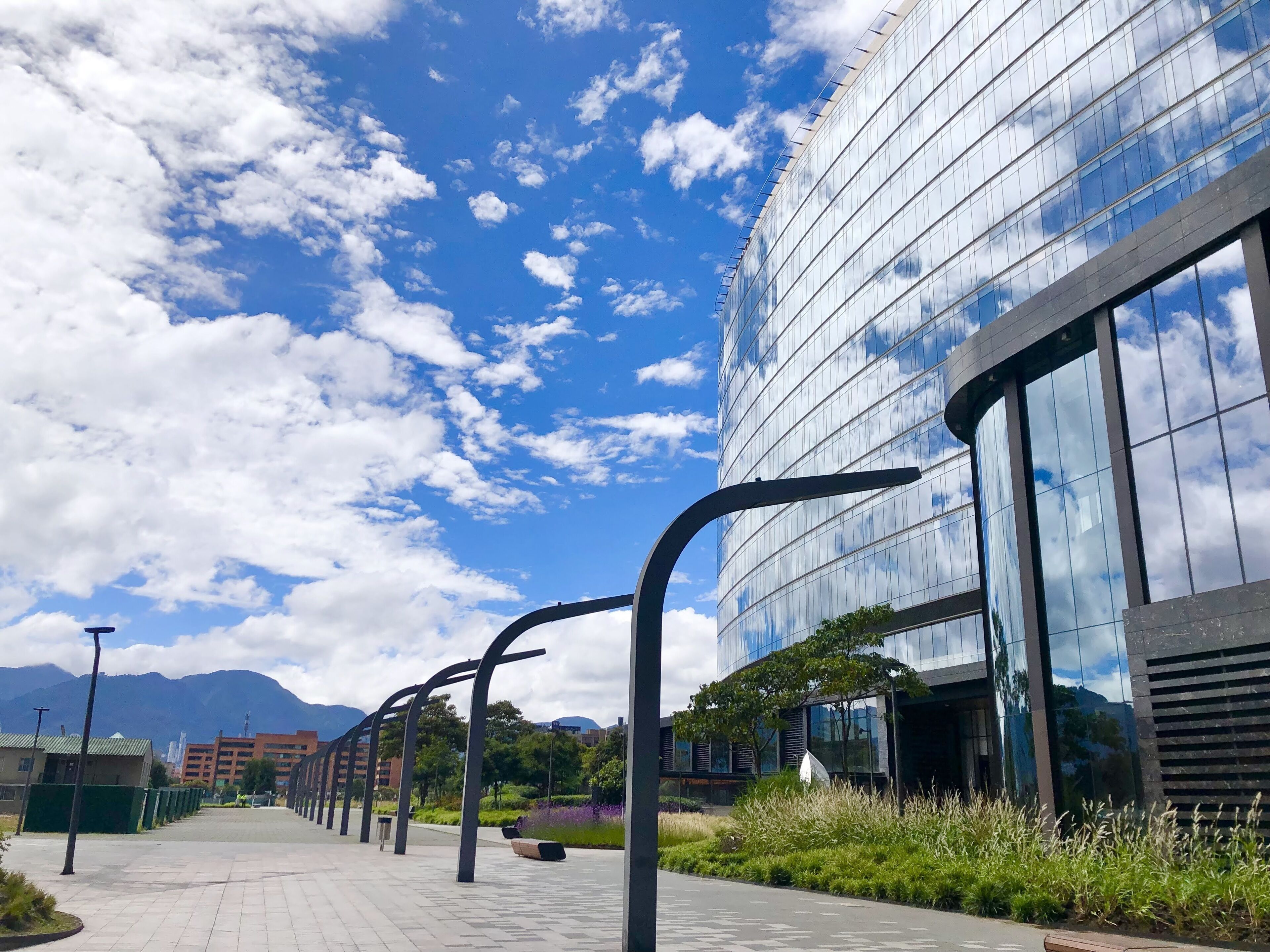 A modern building with reflective glass windows, a paved walkway, and a clear blue sky with clouds.