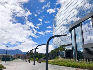 A modern building with reflective glass windows, a paved walkway, and a clear blue sky with clouds. - SalitreCondo (Bogotá)