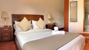 A neatly made bed with a wooden headboard, two bedside tables with lamps, and a mirror on the wall. - SalitreCondo (Bogotá)