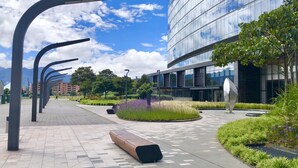 A modern urban plaza with a paved walkway, benches, and a large building with reflective glass windows. - SalitreCondo (Bogotá)