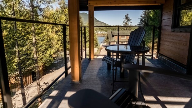 Een houten terras met een tafel en stoelen, met uitzicht op een bos en een meer.