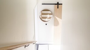 Een smalle, moderne gang met een houten leuning en een ronde spiegel aan de muur.