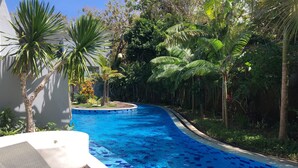 Una piscina con baldosas azules, rodeada de abundante vegetación y palmeras.