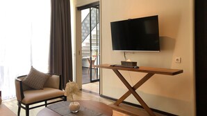 Una sala de estar moderna con un televisor de pantalla plana montado sobre un atril de madera, un sofá cómodo, una pequeña mesa redonda con un florero y una escalera que conduce a un piso superior.
