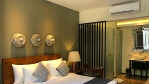 Habitación de hotel con una cama de madera, un escritorio con lámpara, un espejo y un baño visible a través de una puerta.