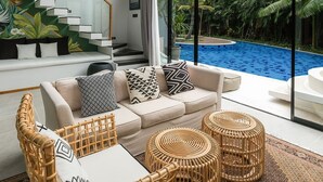 A modern living room with a large glass wall, a staircase, and a pool view. - Inara Villa (Nusa Dua)
