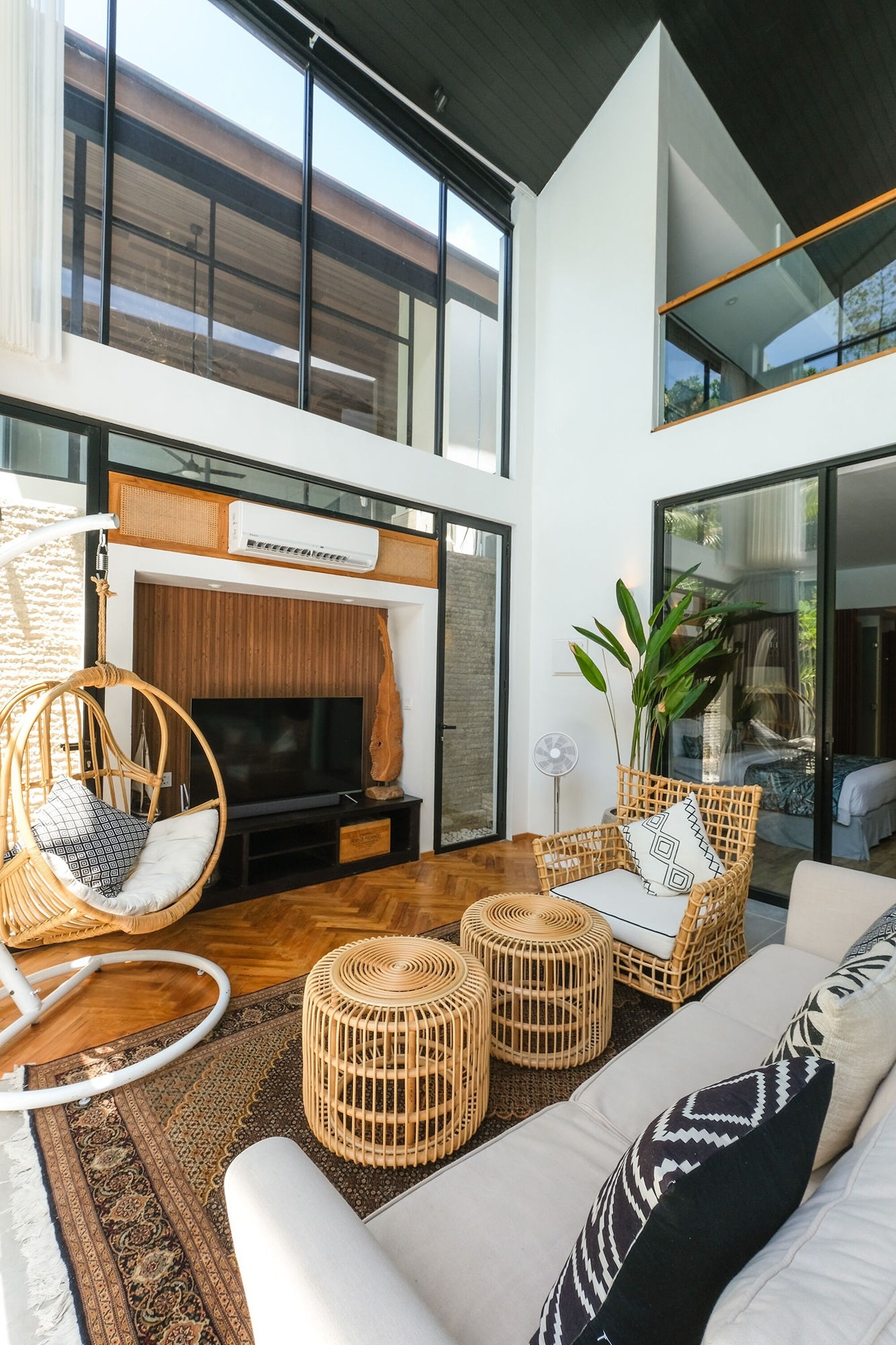 A modern living room with a large TV, wicker furniture, and a view of the outdoors.