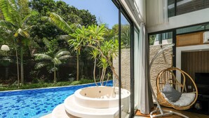 A modern outdoor pool area with a hot tub, a wicker chair, and lush greenery. - Inara Villa (Nusa Dua)