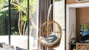 A modern living room with large windows, a sofa, wicker chairs, and a television. - Inara Villa (Nusa Dua)