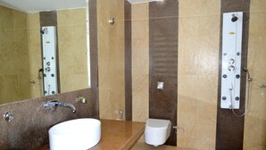 Un baño con lavamanos blanco, espejo, ducha con panel de control y retrete.