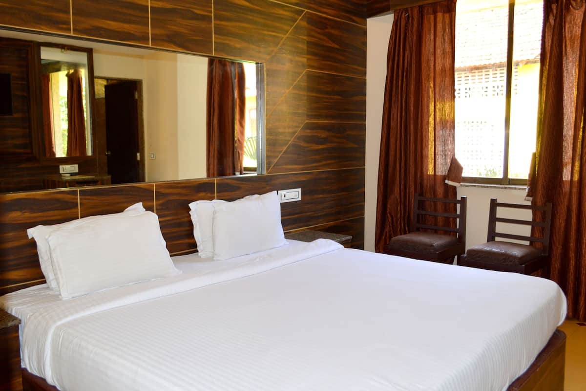 A hotel room with a large bed, a wooden headboard, a mirror, a window with curtains, and a small table with a chair.