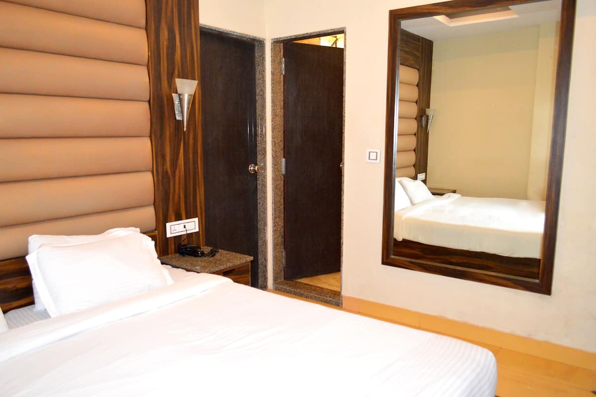 A hotel room with a bed, a bedside table with a phone, a mirror, and a door leading to another room.