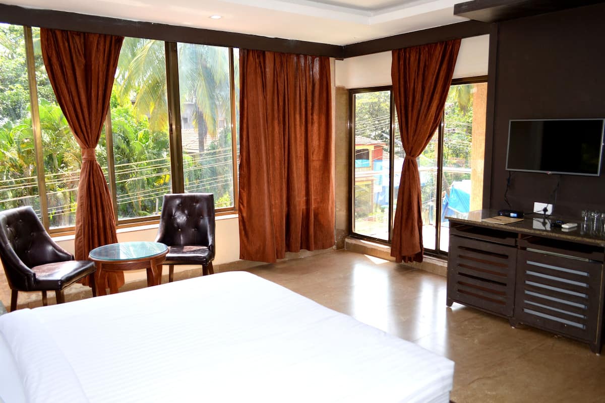 A hotel room with a bed, two chairs, a small table, a TV, and large windows with curtains.