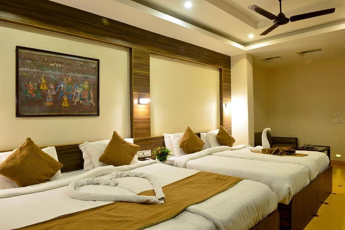 A hotel room with two beds, a ceiling fan, a painting on the wall, and a small table with a plant.