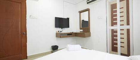 Une chambre d’hôtel comprenant un lit, un téléviseur fixé au mur, une coiffeuse en bois, un miroir et une armoire avec une porte coulissante.