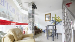 A hotel lobby with a large window, a sofa, a small table with stools, and a decorative plant. - Hotel Pritty (Kuala Lumpur)