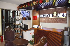 A reception desk with a 'Happy Homes Manila' sign, a television displaying property listings, and a fire extinguisher. - Happy Homes Manila (Manila)