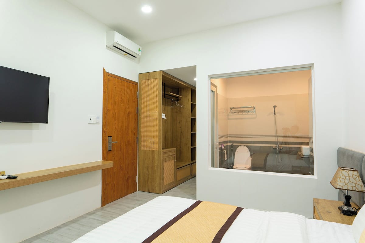 A bedroom with a bed, a TV, a wardrobe, a closet, and a window with a view of a bathroom.