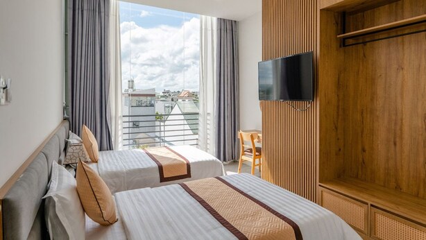 Habitación de hotel con dos camas, un televisor montado en la pared y un balcón con vistas a la ciudad.