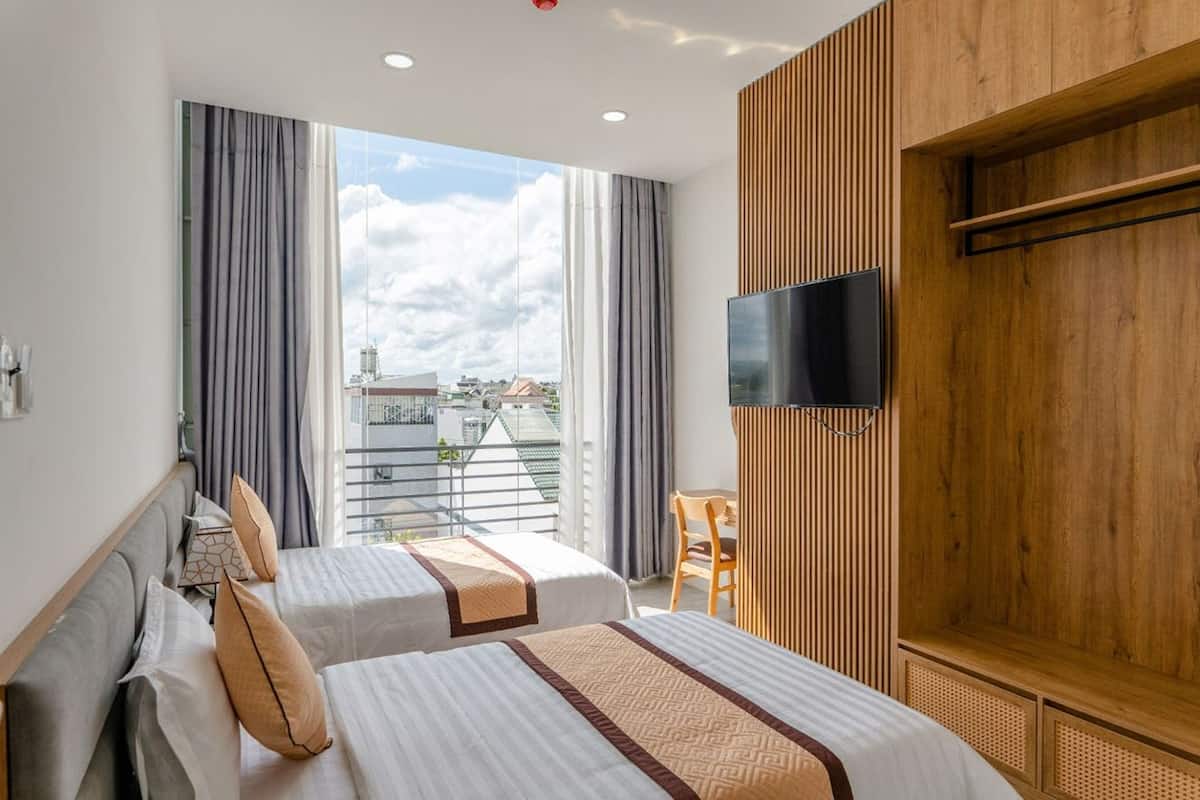 A hotel room with two beds, a TV mounted on the wall, and a balcony with a view of the city.