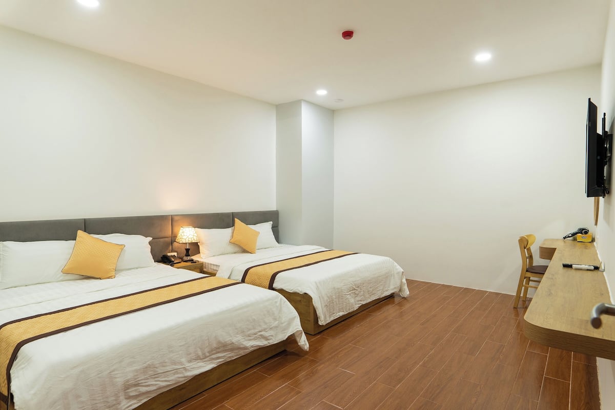 A hotel room with two beds, a desk, a chair, a TV, and a nightstand with a lamp.