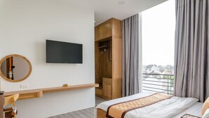 Una habitación de hotel moderna con cama, televisor montado en la pared, escritorio de madera y una ventana grande con cortinas.
