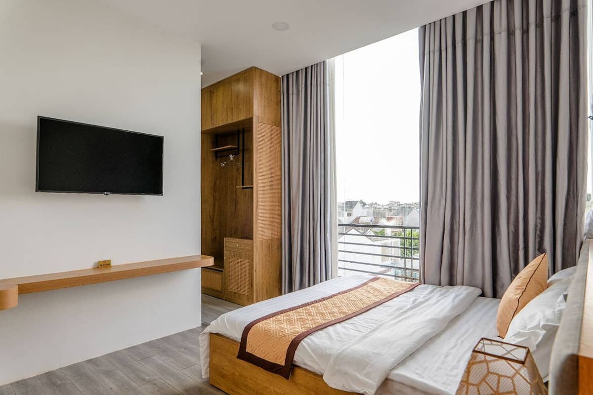 A modern bedroom with a large bed, a mounted TV, a wooden wardrobe, and a balcony view.