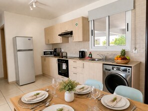 A modern kitchen with a refrigerator, oven, microwave, and dishwasher. There is a dining table set with plates, glasses, and a bowl of fruit.