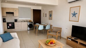 Ein kompakter Wohnraum mit Küchenzeile, Essbereich und einer Sitzecke mit Fernseher und Obstschale.