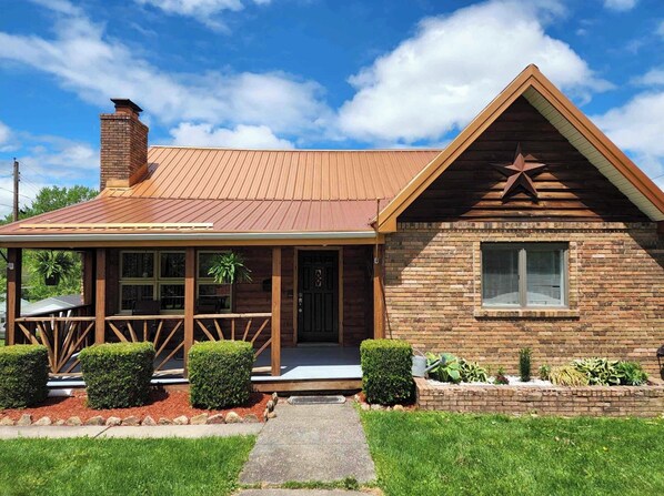 A wooden cabin with a metal roof, a porch with wooden railings, and a star decoration on the front.