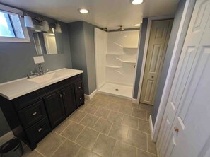 A bathroom with a double sink vanity, a walk-in shower, and a door leading to another room.