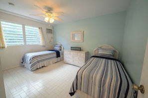 A bedroom with two beds, a ceiling fan, a dresser, and a window with blinds. - 3-bedroom condo w/ amazing Ocean views! (Christiansted)