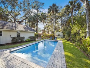 Une piscine rectangulaire bordée d’une allée pavée, entourée d’une pelouse bien entretenue et de divers arbres.