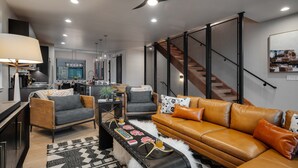 A modern living room with a sofa, chairs, a coffee table, and a kitchen in the background. - Luxurious + Hot Tub on Rooftop Deck + Close to Skiing - Borough House (Steamboat Springs)