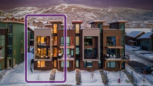 A modern multi-story hotel with a central atrium, large windows, and a view of snow-covered mountains. - Luxurious + Hot Tub on Rooftop Deck + Close to Skiing - Borough House (Steamboat Springs)
