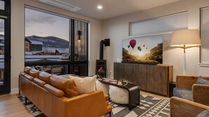 A modern living room with a leather sofa, a wooden coffee table, and a large window offering a scenic mountain view. - Luxurious + Hot Tub on Rooftop Deck + Close to Skiing - Borough House (Steamboat Springs)