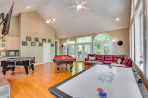 Una habitación amplia con mesa de billar, mesa de fútbol de mesa y un sofá de cuero rojo.