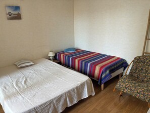 Ein Zimmer mit zwei Betten, einem Sessel, einer Lampe und einem Wandbild.