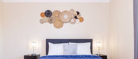 A bedroom with a large bed, two bedside tables, a wall art piece, and a folded towel on the bed.