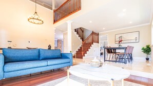A spacious living room with a blue sofa, a white coffee table, and a staircase leading to an upper level. - Maison du Lavande, artzy 4Br House, gateway 2 Napa (Vallejo)