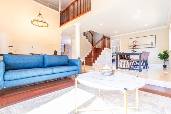 Un salón amplio con un sofá azul, una mesa de centro blanca y una escalera que conduce a un nivel superior.