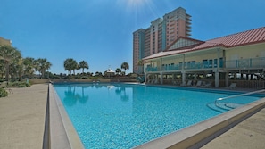 A swimming pool with a clear blue water, surrounded by lounge chairs and a building with balconies.