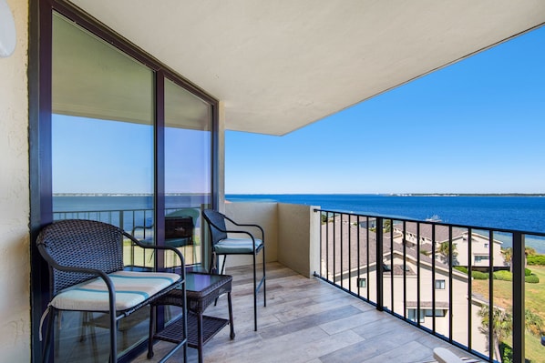 A balcony with two wicker chairs and a small table, overlooking a beach and ocean. - 🌟Gorgeous Updates-Sound Views-Steps2Beach-Pool-1BR Santa Rosa Dunes 1063🌟 (Pensacola Beach)