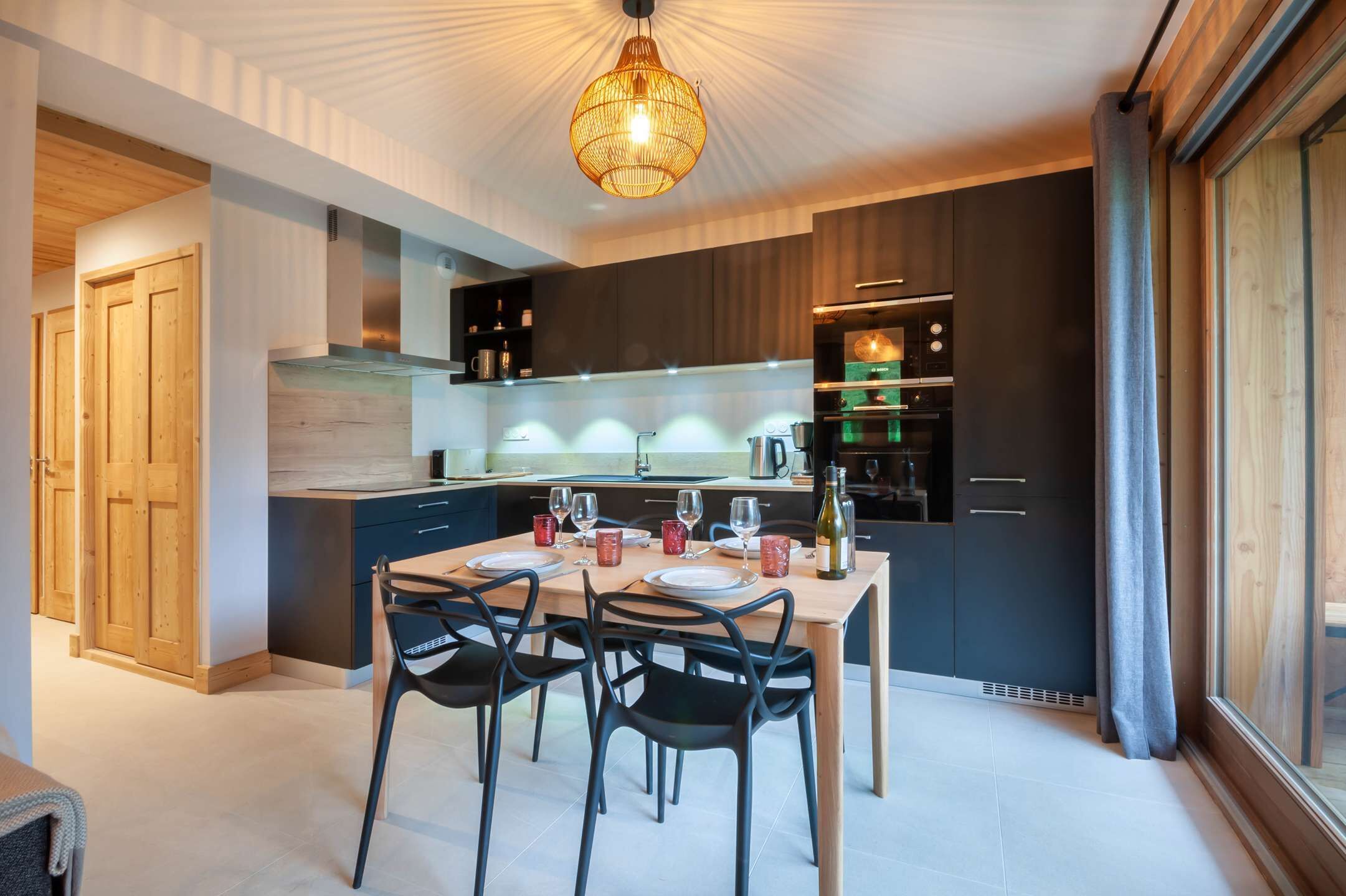 Una cucina moderna con mobili scuri, un tavolo da pranzo in legno e sedie nere.