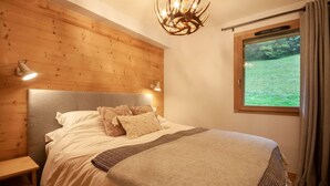 Un dormitorio con cabecera de madera, una cama grande con ropa blanca, dos lámparas de noche y una ventana con vistas a zonas verdes.