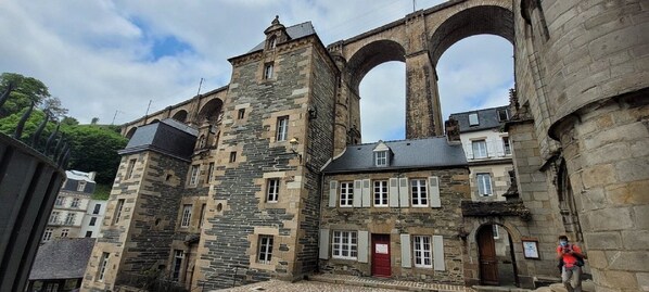A historic stone building with arched windows and a red door, surrounded by other buildings.