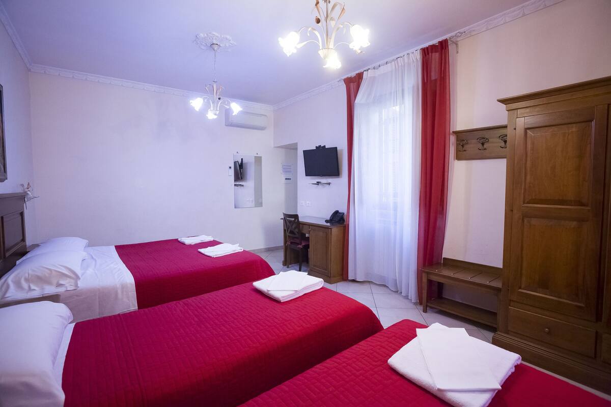 Habitación de hotel con tres camas, un escritorio, una silla, un televisor y un armario.