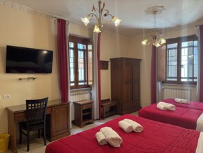 Une chambre d’hôtel équipée d’une télévision, d’un bureau, d’une chaise, d’une armoire, d’un lit avec une literie rouge et d’un lustre.